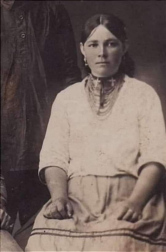 Жінка на світлині має намисто з дрібних коралів, до якого підвішені два срібних хрестики. Її образ доповнюють срібні сережки "пташечки"